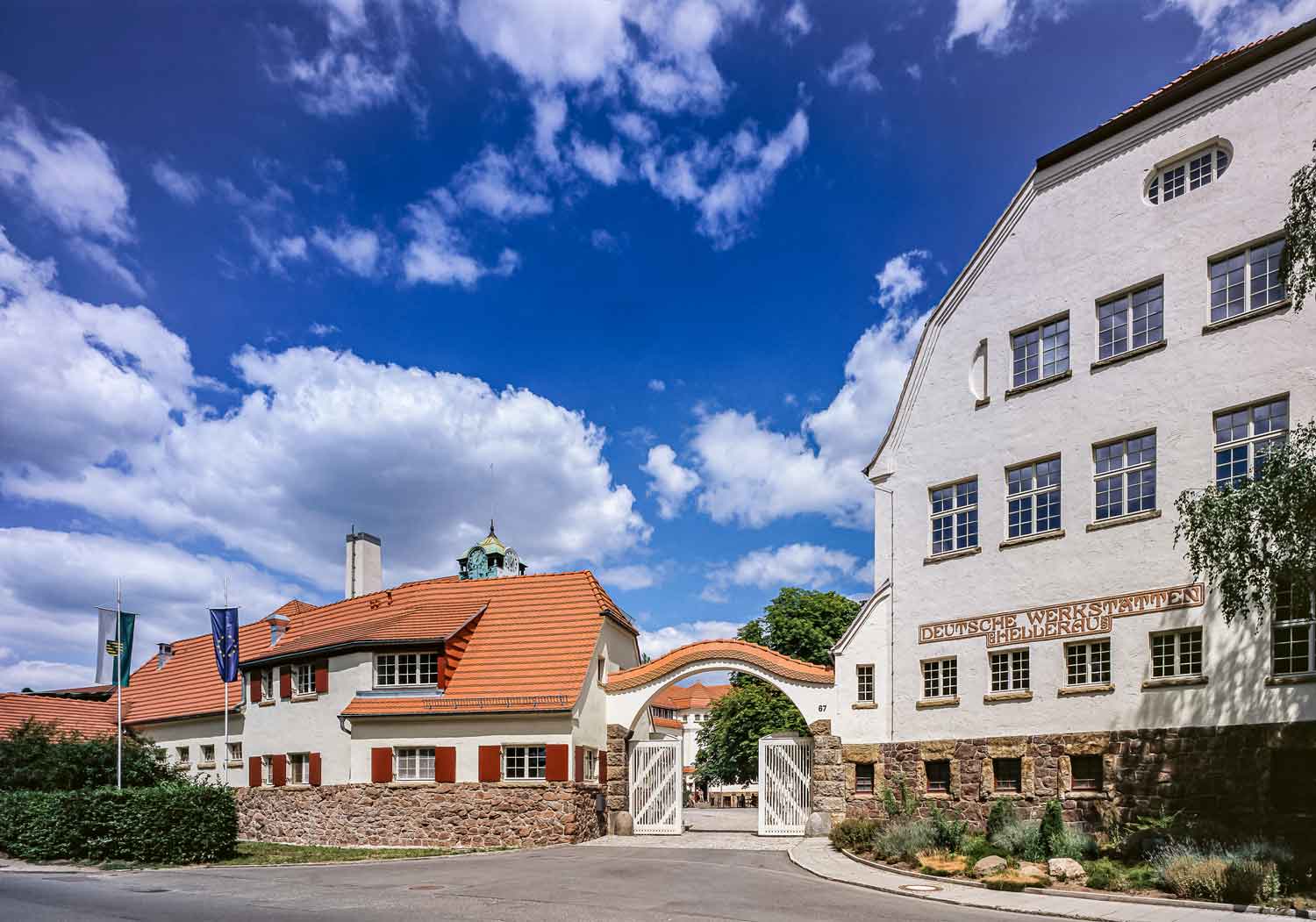 Foto, farbig: Eingangstor mit geschwungenem Bogen, links und rechts ein Gebäude.