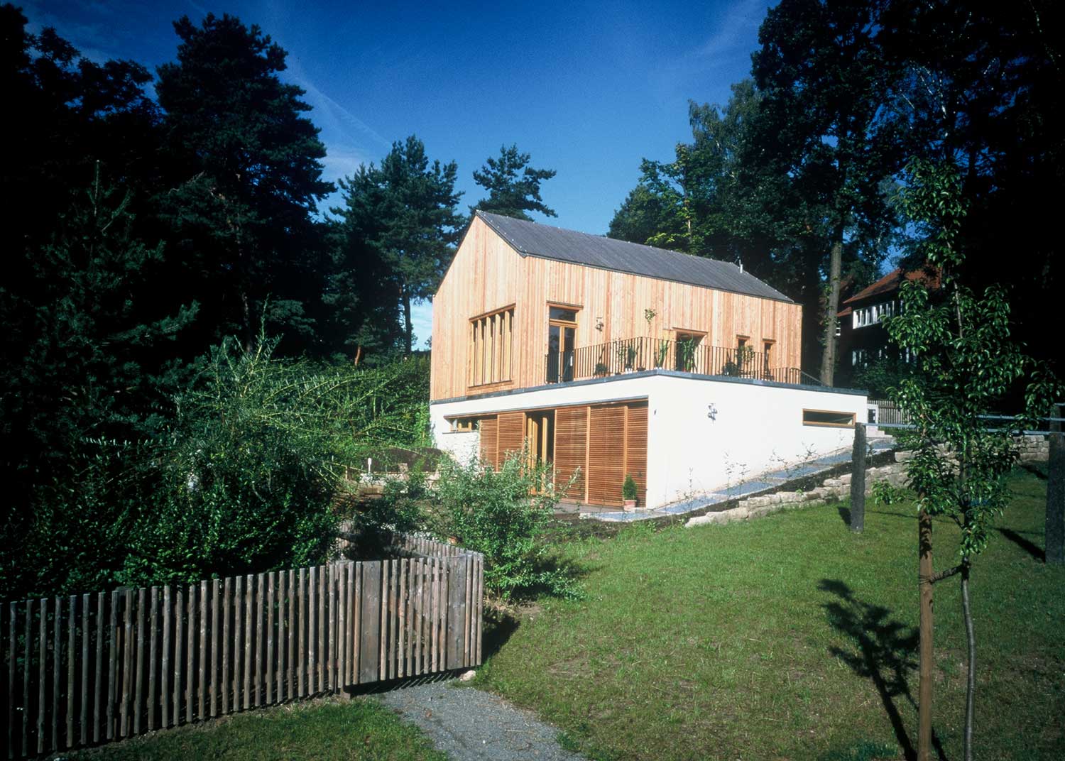 Foto, farbig: Holzhaus mit schmalen Fenstern auf einem weißen Untergeschoss mit großen Türen aus Holzlamellen.