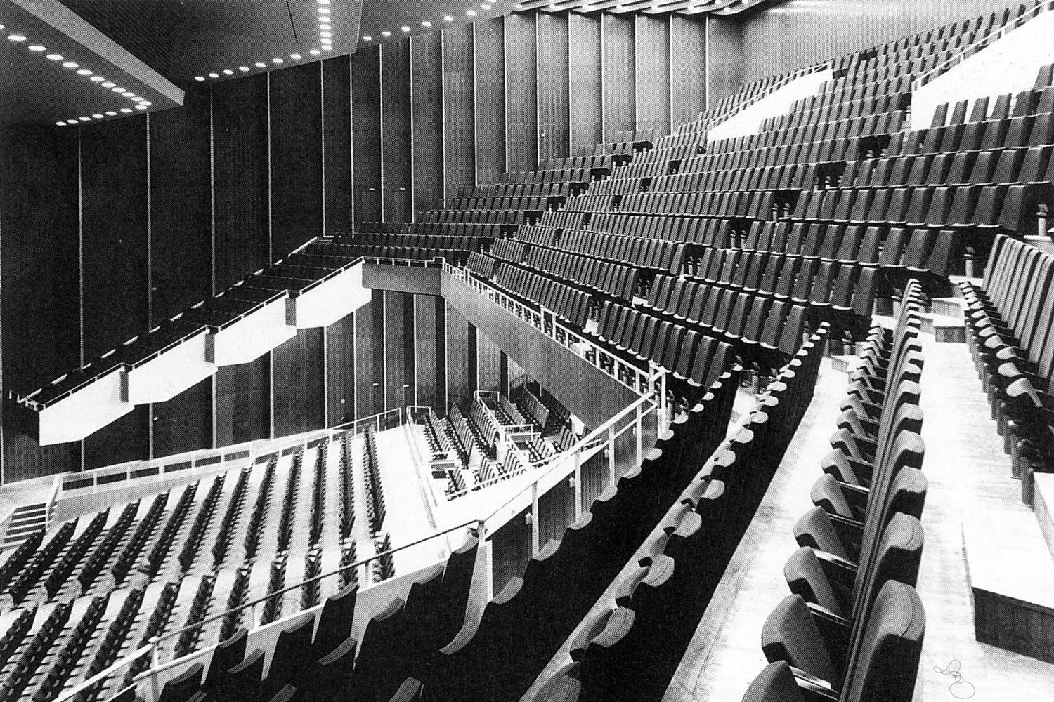 Foto, schwarz-weiß: Blick in den leeren Zuschauerraum mit ansteigenden Reihen aus Klappsitzen.