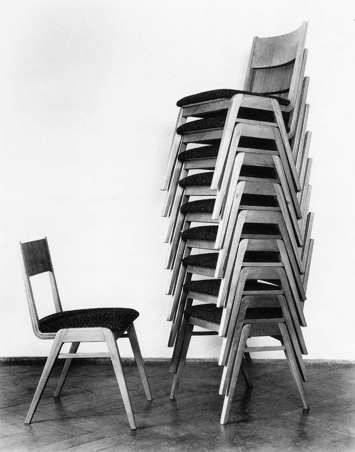 Foto, schwarz-weiß: Links ein einzelner Stuhl, rechts ein Turm aus neun ineinander gestapelten Stühlen.